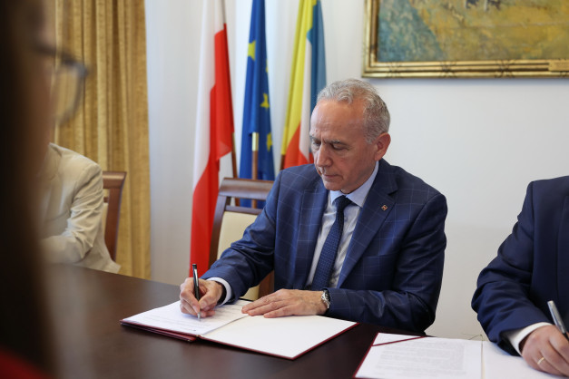 Mężczyzna w garniturze podpisuje dokument. W tle flagi Polski, UE i Ukrainy.