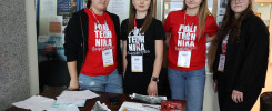 Cztery młode kobiety w koszulkach z napisem "POLITECHNIKA Świętokrzyska" stoją przy stole z materiałami informacyjnymi.