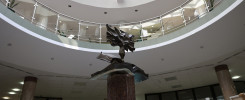 Rzeźba na postumencie w atrium budynku, otoczona galeriami z balustradami i sztalugami.