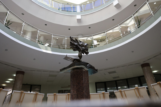 Rzeźba na postumencie w atrium budynku, otoczona galeriami z balustradami i sztalugami.
