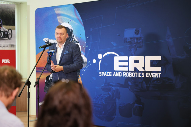 Mężczyzna w garniturze przemawia przy mikrofonie. Tło to baner "ERC SPACE AND ROBOTICS EVENT".