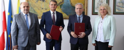 Cztery osoby stoją przed obrazem. Dwie osoby trzymają dokumenty.