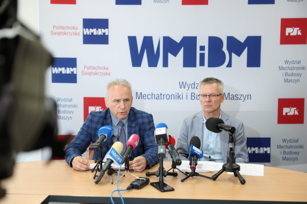Dwóch mężczyzn siedzi przy stole z mikrofonami. W tle logo Politechniki Świętokrzyskiej.