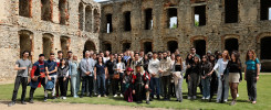 Grupa ludzi pozuje do zdjęcia na tle ruin zamku. Wśród nich są osoby w strojach historycznych.