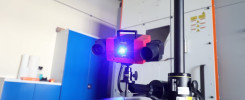 Czerwony skaner 3D z niebieskim światłem, zamontowany na statywie, w pomieszczeniu laboratoryjnym.