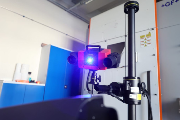Czerwony skaner 3D z niebieskim światłem, zamontowany na statywie, w pomieszczeniu laboratoryjnym.