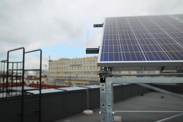 Panel fotowoltaiczny na dachu, widok na budynek i drabinkę. Kontekst: miejski, instalacja OZE.