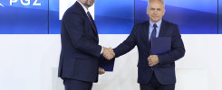 Dwóch mężczyzn w garniturach ściska sobie dłonie. Trzymają teczki. W tle logo PGZ.