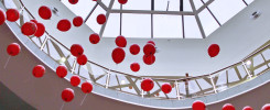 Czerwone balony unoszą się pod przeszklonym sufitem centrum handlowego. Widoczne balony, balustrady, okna.