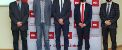 Pięciu mężczyzn w garniturach i z maskami na twarzach stoi przed banerem Politechniki Świętokrzyskiej.