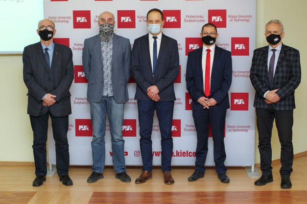 Pięciu mężczyzn w garniturach i z maskami na twarzach stoi przed banerem Politechniki Świętokrzyskiej.