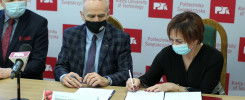Trzy osoby w maseczkach siedzą przy stole, podpisując dokumenty. W tle logo Politechniki Świętokrzyskiej.