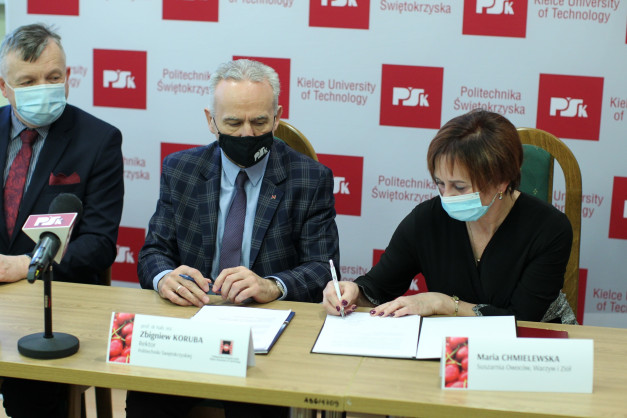 Trzy osoby w maseczkach siedzą przy stole, podpisując dokumenty. W tle logo Politechniki Świętokrzyskiej.