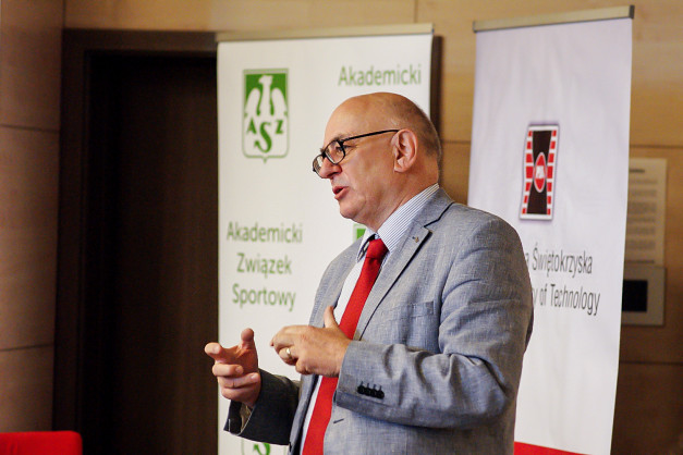 Mężczyzna w garniturze i krawacie przemawia. W tle banery z logo "Akademicki Związek Sportowy" i Politechniki Świętokrzyskiej.