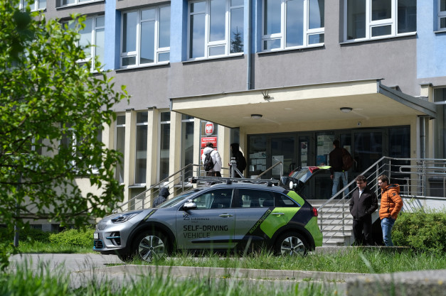 Srebrny samochód autonomiczny z napisem "SELF-DRIVING VEHICLE" stoi przed budynkiem.