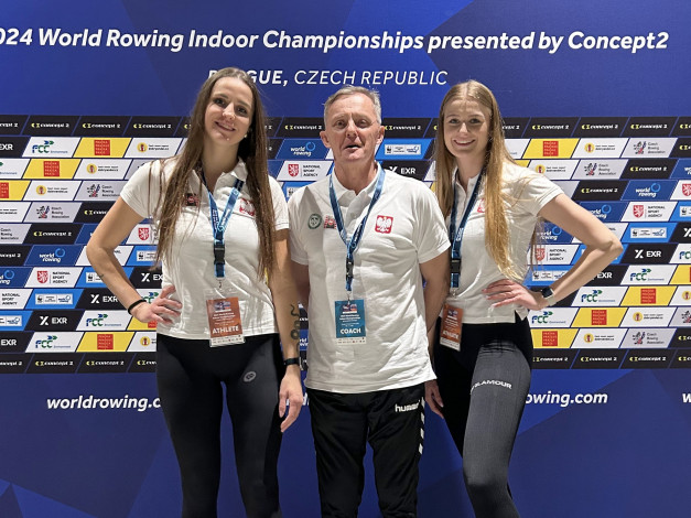 Trzy osoby w białych koszulkach z polskimi symbolami na tle baneru "2024 World Rowing Indoor Championships".