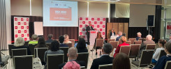 Konferencja BSD 2022. Mężczyzna przemawia na podium, widownia siedzi. Kluczowe obiekty: podium, ekran, widownia.