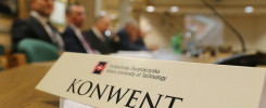 Tabliczka z napisem "KONWENT" i logo Politechniki Świętokrzyskiej. W tle siedzą mężczyźni w garniturach.