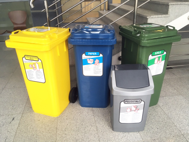 Cztery kosze do segregacji: żółty (tworzywa sztuczne), niebieski (papier), zielony (szkło) i szary (pozostałe).