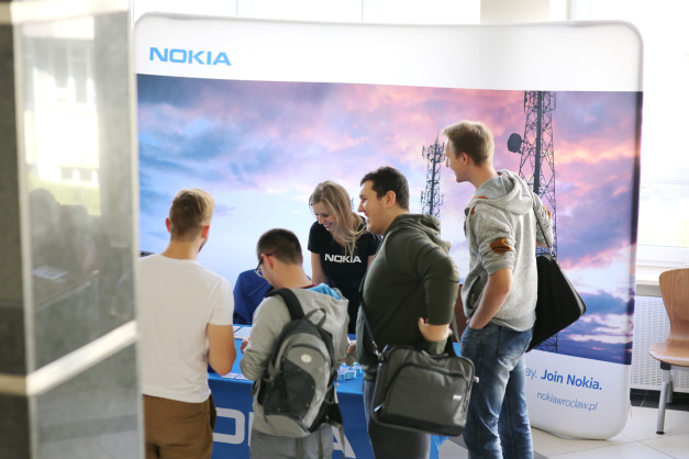 Ludzie przy stoisku Nokia. Tło z logiem Nokia i zdjęciem masztów telekomunikacyjnych.