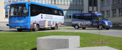 Dwa niebieskie pojazdy, autobus i bus, stoją przed budynkiem uniwersyteckim.