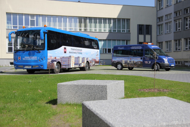 Dwa niebieskie pojazdy, autobus i bus, stoją przed budynkiem uniwersyteckim.