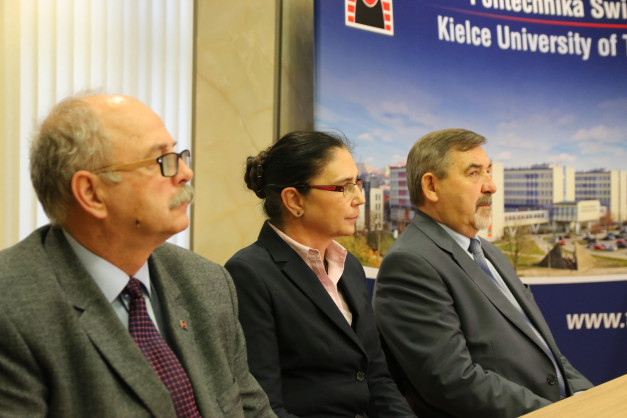 Trzy osoby w garniturach siedzą przy stole. W tle baner z logo Politechniki Świętokrzyskiej.