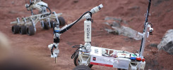 Dwa roboty terenowe z ramionami i flagami Polski. Jeden z nich ma napis "IMPULS II". Kontekst: zawody robotów.