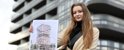 Kobieta trzyma wizualizację nowoczesnego budynku. W tle widać architekturę miejską.