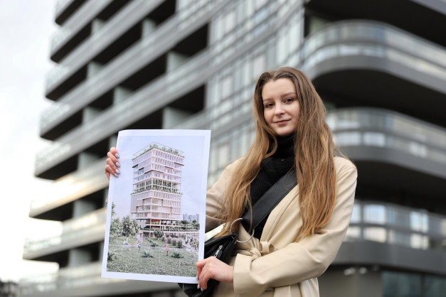 Kobieta trzyma wizualizację nowoczesnego budynku. W tle widać architekturę miejską.