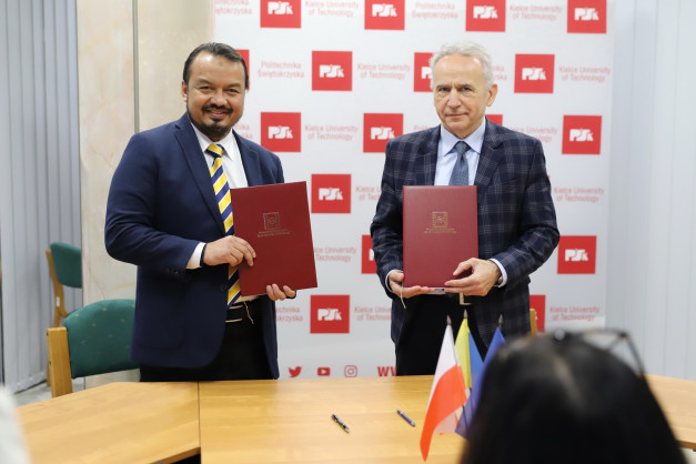 Dwóch mężczyzn w garniturach trzyma czerwone teczki. W tle logo Politechniki Świętokrzyskiej.