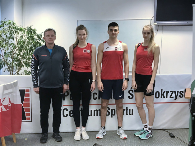 Cztery osoby w strojach sportowych stoją przed tablicą. Kluczowe obiekty: mężczyzna, trzy kobiety, stroje sportowe, tablica.
