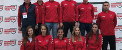 Grupa osób w czerwonych bluzach z logo "Akademickie Mistrzostwa Polski". W tle biała ściana z powtarzającym się logo.