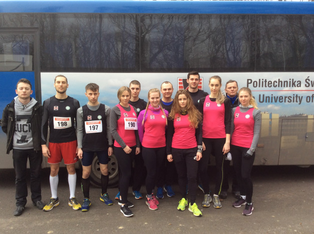 Grupa ludzi w strojach sportowych stoi przed autobusem z napisem "Politechnika Śląska".