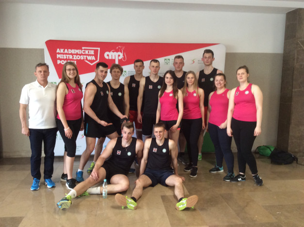 Grupa sportowców pozuje do zdjęcia na tle banera "Akademickie Mistrzostwa Polski".