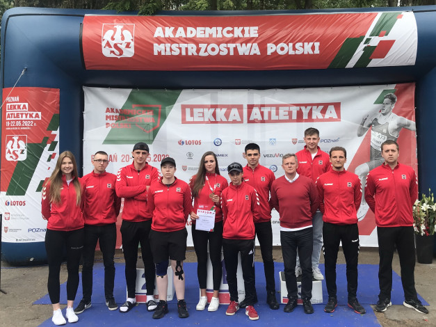 Grupa sportowców w czerwonych strojach pozuje na tle baneru "Akademickie Mistrzostwa Polski".