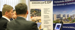 Mężczyźni w garniturach siedzą przy stole, przed nimi baner z logo uczelni i napisem "KONSORCJUM COP".