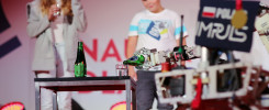Robot nalewa płyn z butelki do szklanki. W tle dziewczyna i chłopiec.