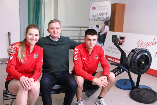 Trzy osoby siedzą na ławce wioślarskiej. W tle baner Politechniki Świętokrzyskiej.