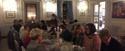 Ludzie siedzą przy stole w restauracji, jedząc i rozmawiając. Kluczowe obiekty: stół, jedzenie, ludzie, świece.