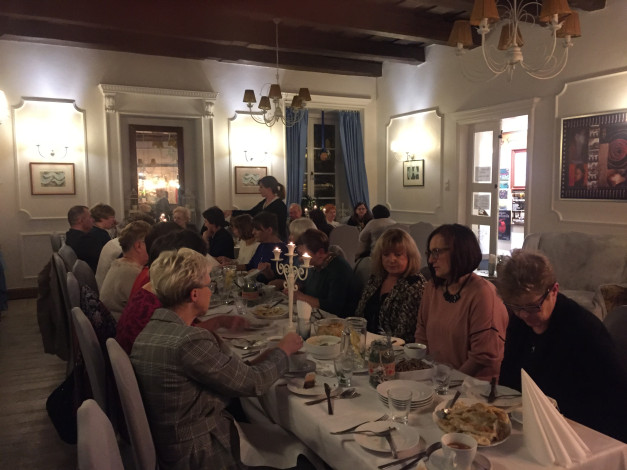 Ludzie siedzą przy stole w restauracji, jedząc i rozmawiając. Kluczowe obiekty: stół, jedzenie, ludzie, świece.