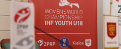 Czerwony baner z napisem "Women's World Championship IHF Youth U18". W tle widoczne flagi i logo ZPRP.