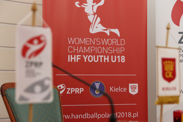 Czerwony baner z napisem "Women's World Championship IHF Youth U18". W tle widoczne flagi i logo ZPRP.