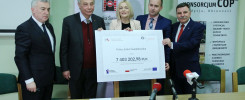 Cztery osoby stoją za stołem, trzymając czek na kwotę 7 403 202,98 PLN. Kontekst to wręczenie grantu.