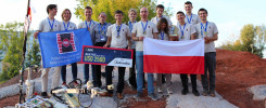 Grupa młodych ludzi z Politechniki Świętokrzyskiej świętuje wygraną z robotem. Kluczowe obiekty: robot, flagi, nagrody.