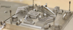 Metalowe wydruki 3D, w tym elementy zębate i kształty geometryczne, na metalowej płycie.