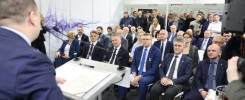 Mężczyzna w garniturze przemawia do zgromadzonych osób. W tle widać uczestników wydarzenia.