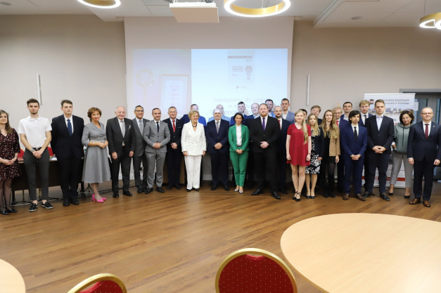 Grupa osób pozuje do zdjęcia w sali konferencyjnej. W tle ekran z napisem "Politechnika Świętokrzyska".