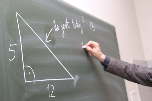 Trójkąt prostokątny z bokami 5 i 12. Ręka pisze kredą na tablicy. Kontekst: lekcja matematyki.