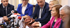 Ludzie przy stole z mikrofonami. Konferencja prasowa.